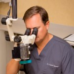 Endodontist Dr. Tancreto looking through a dental instrument at {PRACTICE_NAME}