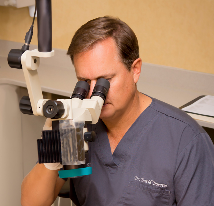 Endodontist Dr. Tancreto looking through a dental instrument at {PRACTICE_NAME}
