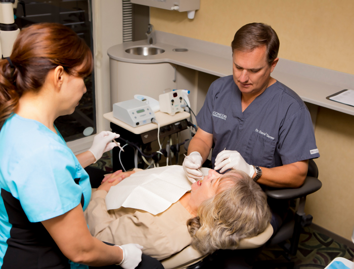 Endodontist Dr. Tancreto and a dental assistant working on a patient in the examination room at {PRACTICE_NAME}