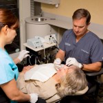 Endodontist Dr. Tancreto and a dental assistant working on a patient in the examination room at {PRACTICE_NAME}